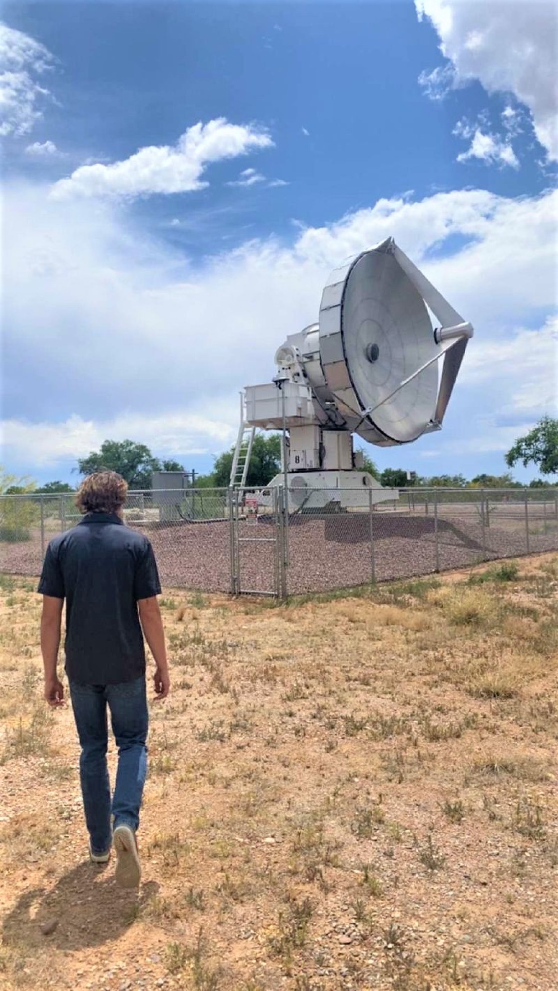 Young man walking toward large radio antenna