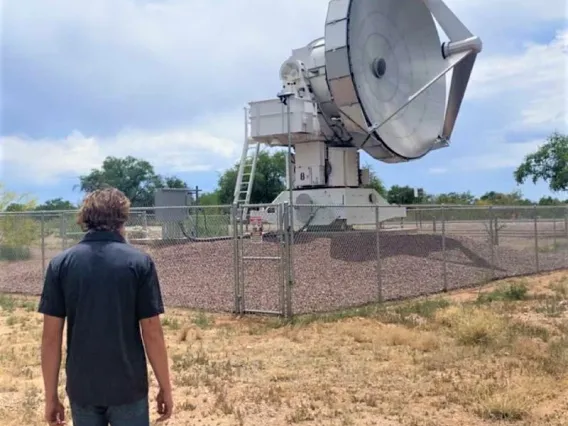 Intern Chance Lawrence walking toward Rincon Research Corporation's 6.1meter millimeter-wave antenna